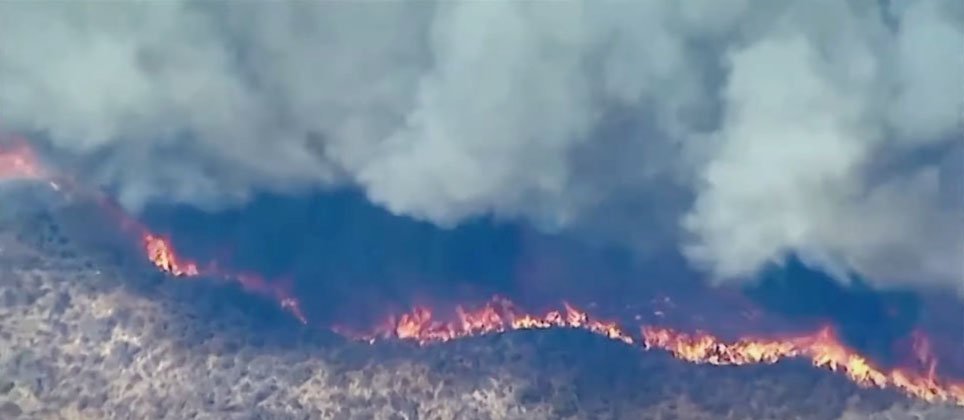 Aerial view of the Hughes Fire in Southern California showing widespread wildfire damage, thick smoke, and evacuation efforts.