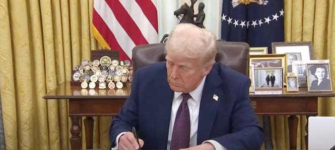 Former President Donald Trump signing a document to impose new tariffs on China, Mexico, and Canada, with officials and reporters in the background.
